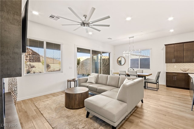 living room with plenty of natural light, light hardwood / wood-style flooring, and ceiling fan with notable chandelier