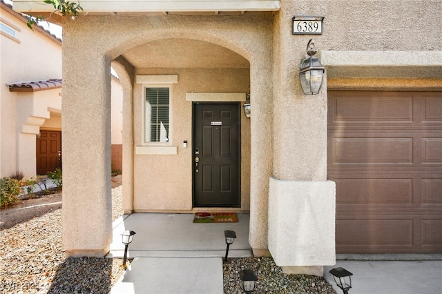 view of exterior entry featuring an attached garage and stucco siding