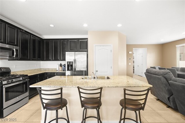 kitchen with appliances with stainless steel finishes, sink, an island with sink, a breakfast bar area, and light tile patterned flooring