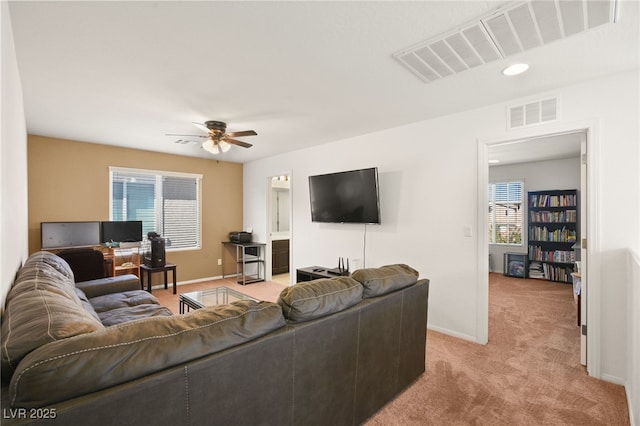 living area featuring ceiling fan, a healthy amount of sunlight, visible vents, and light carpet