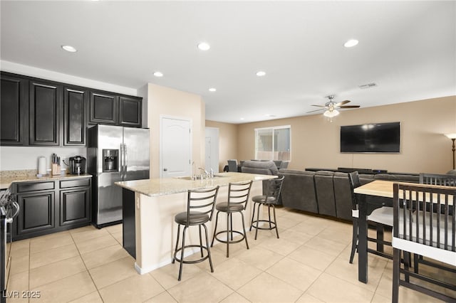 kitchen featuring visible vents, stainless steel fridge with ice dispenser, an island with sink, dark cabinetry, and a sink