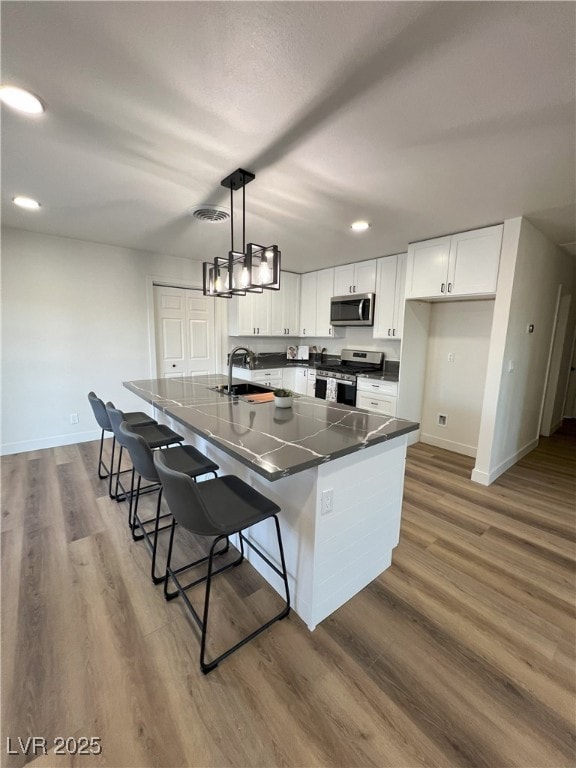 kitchen with white cabinets, hanging light fixtures, stainless steel appliances, and a large island with sink