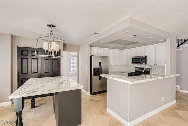 kitchen with hanging light fixtures, appliances with stainless steel finishes, white cabinetry, light stone counters, and kitchen peninsula