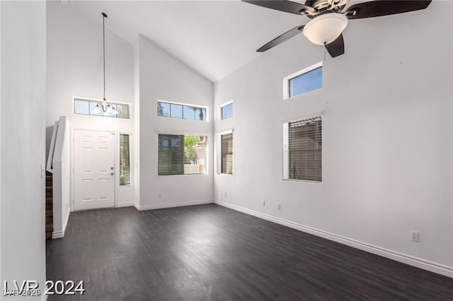 unfurnished living room with high vaulted ceiling, dark wood-type flooring, and ceiling fan with notable chandelier