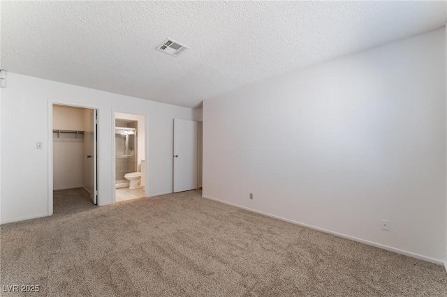 unfurnished bedroom featuring a textured ceiling, light colored carpet, a spacious closet, connected bathroom, and a closet