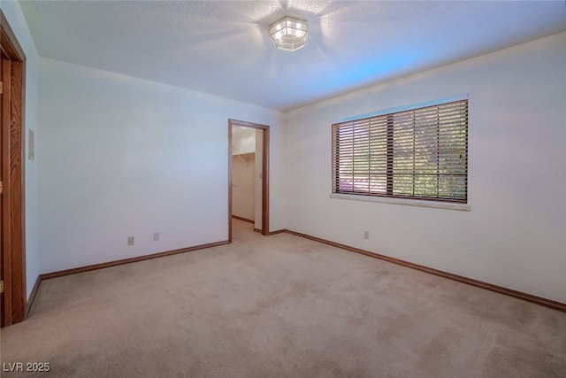 spare room with light carpet, a textured ceiling, and baseboards