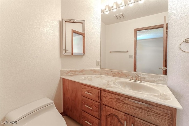 bathroom with visible vents, a textured wall, vanity, and toilet