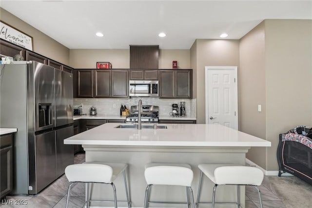 kitchen featuring dark brown cabinetry, sink, stainless steel appliances, a kitchen breakfast bar, and an island with sink