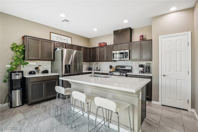 kitchen featuring sink, stainless steel appliances, a kitchen bar, a kitchen island with sink, and dark brown cabinets