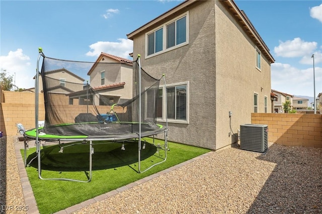 rear view of house featuring a lawn, cooling unit, and a trampoline