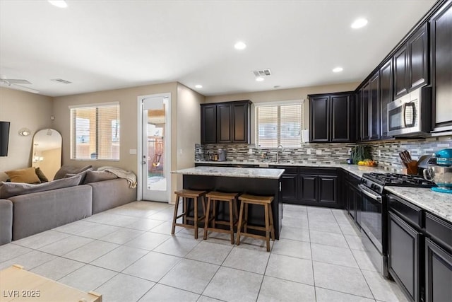 kitchen featuring a breakfast bar area, light stone countertops, a center island, and appliances with stainless steel finishes