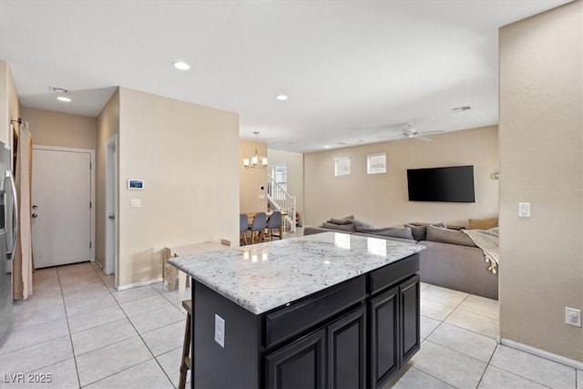 kitchen with pendant lighting, a center island, a kitchen breakfast bar, ceiling fan with notable chandelier, and light tile patterned flooring