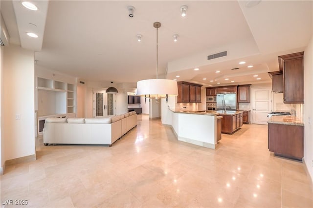 kitchen featuring pendant lighting, built in shelves, a large island, light stone counters, and stainless steel appliances