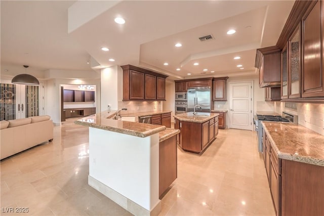 kitchen featuring kitchen peninsula, decorative backsplash, sink, built in appliances, and an island with sink