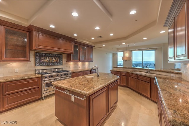 kitchen with stainless steel range, a center island with sink, hanging light fixtures, and sink