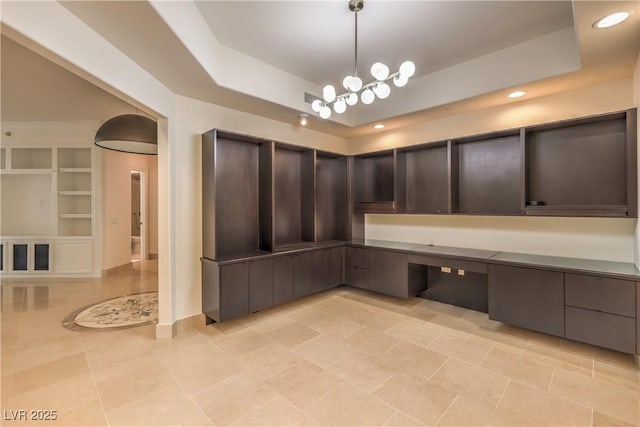 unfurnished office with built in shelves, light tile patterned flooring, a raised ceiling, and a chandelier