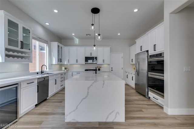 kitchen with a center island, light stone countertops, decorative light fixtures, stainless steel appliances, and beverage cooler