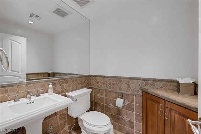 bathroom featuring toilet, tile walls, and sink