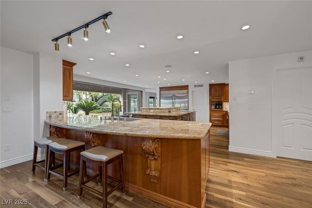 kitchen featuring a kitchen breakfast bar, sink, kitchen peninsula, light stone counters, and wood-type flooring