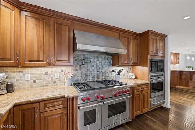 kitchen featuring wall chimney exhaust hood, stainless steel appliances, tasteful backsplash, light stone counters, and dark hardwood / wood-style flooring