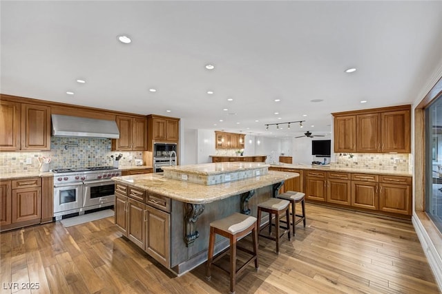 kitchen featuring light stone countertops, an island with sink, range with two ovens, a breakfast bar, and exhaust hood