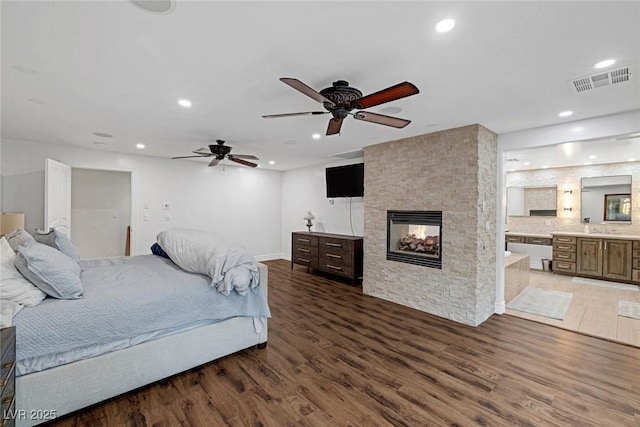 bedroom with dark hardwood / wood-style floors, ensuite bath, ceiling fan, and a stone fireplace