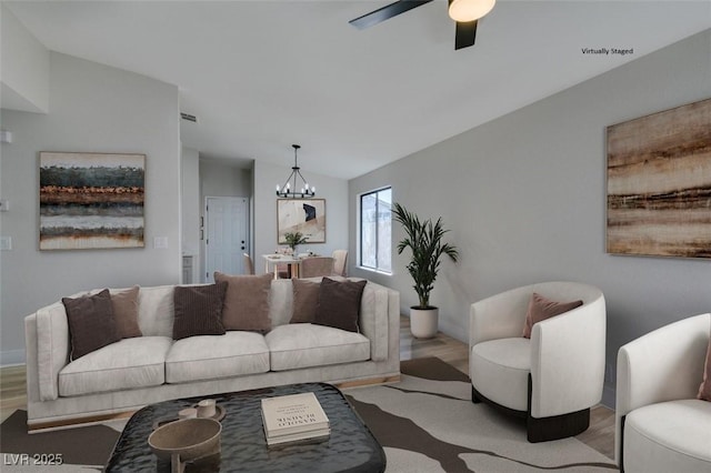 living room with ceiling fan with notable chandelier, light hardwood / wood-style flooring, and vaulted ceiling