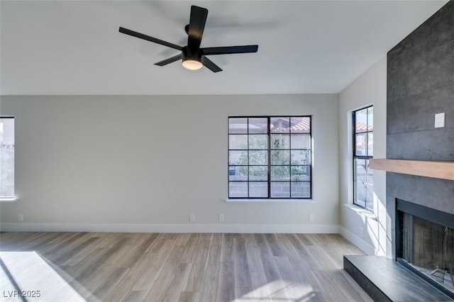 unfurnished living room featuring ceiling fan, a large fireplace, and light hardwood / wood-style flooring