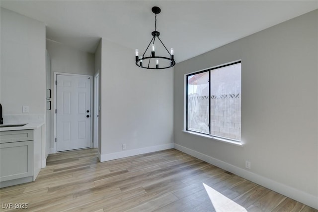 unfurnished dining area with sink, light hardwood / wood-style flooring, and a chandelier