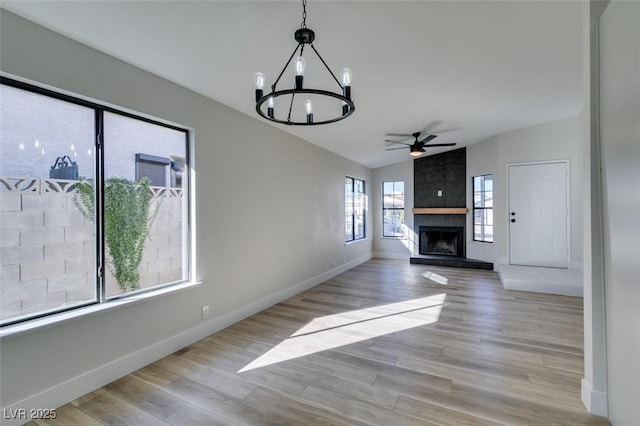 unfurnished living room with ceiling fan with notable chandelier, light wood-type flooring, a fireplace, and vaulted ceiling