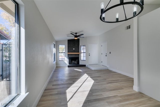 unfurnished living room with ceiling fan with notable chandelier, light hardwood / wood-style floors, and a large fireplace