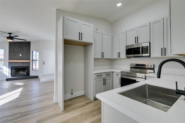 kitchen with ceiling fan, sink, stainless steel appliances, light hardwood / wood-style flooring, and a fireplace