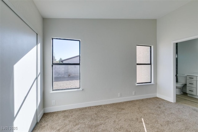 unfurnished bedroom with connected bathroom, light carpet, and lofted ceiling