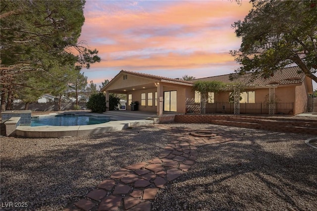 pool at dusk with a hot tub and a patio area