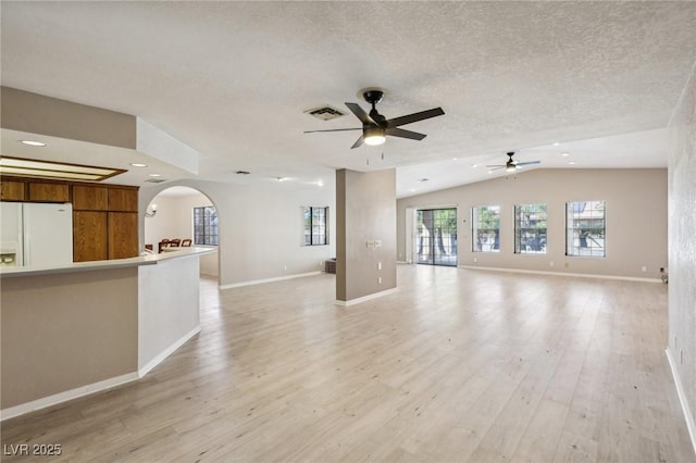 unfurnished living room with vaulted ceiling, a textured ceiling, ceiling fan, and light hardwood / wood-style floors