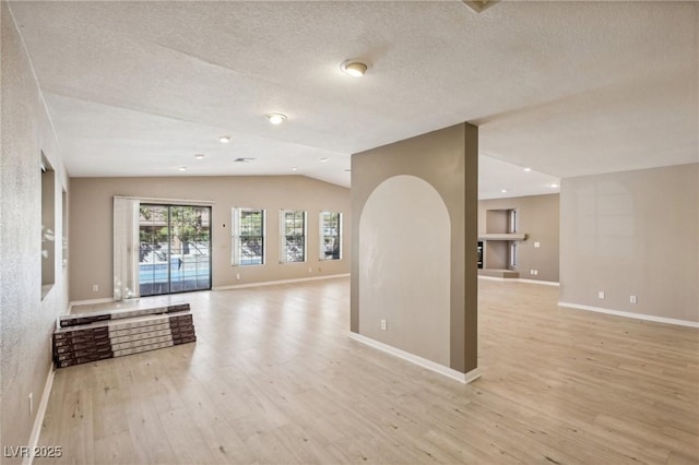 unfurnished room with light hardwood / wood-style floors, lofted ceiling, and a textured ceiling