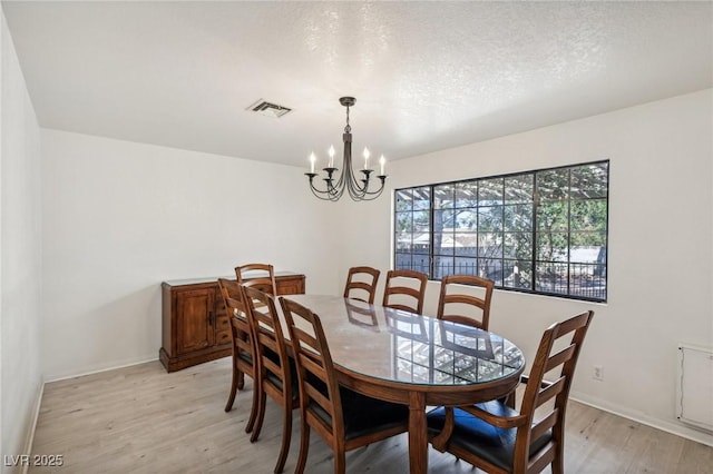 dining area with an inviting chandelier, light wood-type flooring, and a textured ceiling