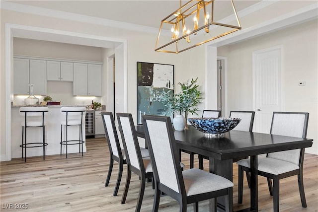 dining area with a chandelier, ornamental molding, beverage cooler, and light hardwood / wood-style flooring