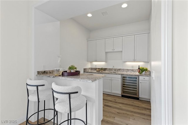 kitchen featuring white cabinets, light hardwood / wood-style floors, light stone counters, kitchen peninsula, and beverage cooler