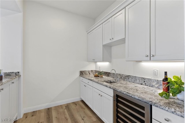 kitchen featuring light stone counters, sink, white cabinets, and beverage cooler