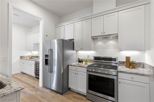 kitchen featuring white cabinets, wine cooler, light hardwood / wood-style flooring, light stone countertops, and appliances with stainless steel finishes