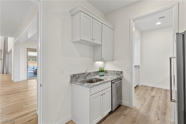 kitchen with light stone counters, stainless steel appliances, white cabinetry, and sink