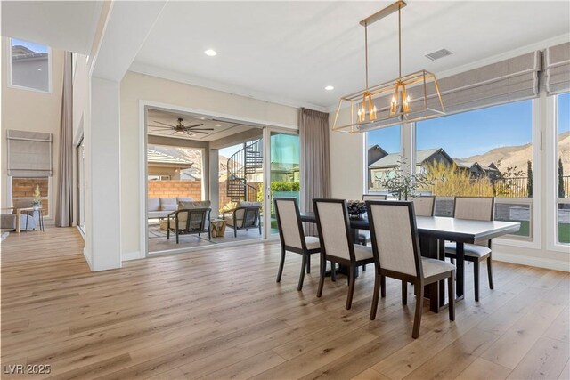 dining room featuring a mountain view, light hardwood / wood-style flooring, ceiling fan with notable chandelier, and ornamental molding