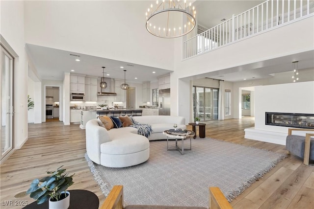 living room with a high ceiling, an inviting chandelier, and light hardwood / wood-style flooring