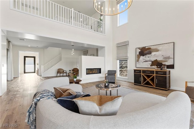 living room featuring a towering ceiling, a chandelier, and light wood-type flooring