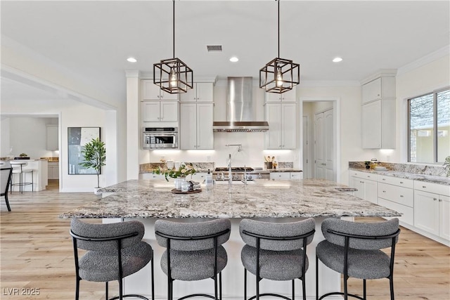 kitchen with stainless steel oven, wall chimney range hood, pendant lighting, a spacious island, and white cabinets