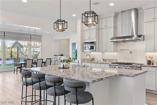 kitchen featuring sink, wall chimney exhaust hood, an island with sink, and decorative light fixtures