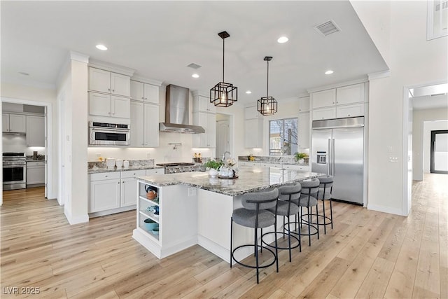 kitchen featuring light stone countertops, appliances with stainless steel finishes, wall chimney exhaust hood, a kitchen island, and white cabinetry