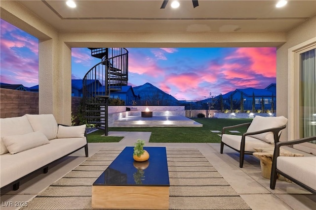 patio terrace at dusk featuring a lawn, outdoor lounge area, and ceiling fan