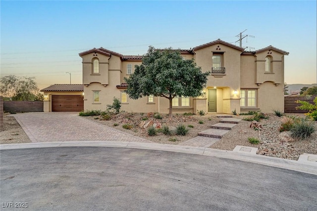 mediterranean / spanish home featuring fence, stucco siding, a garage, a tiled roof, and decorative driveway